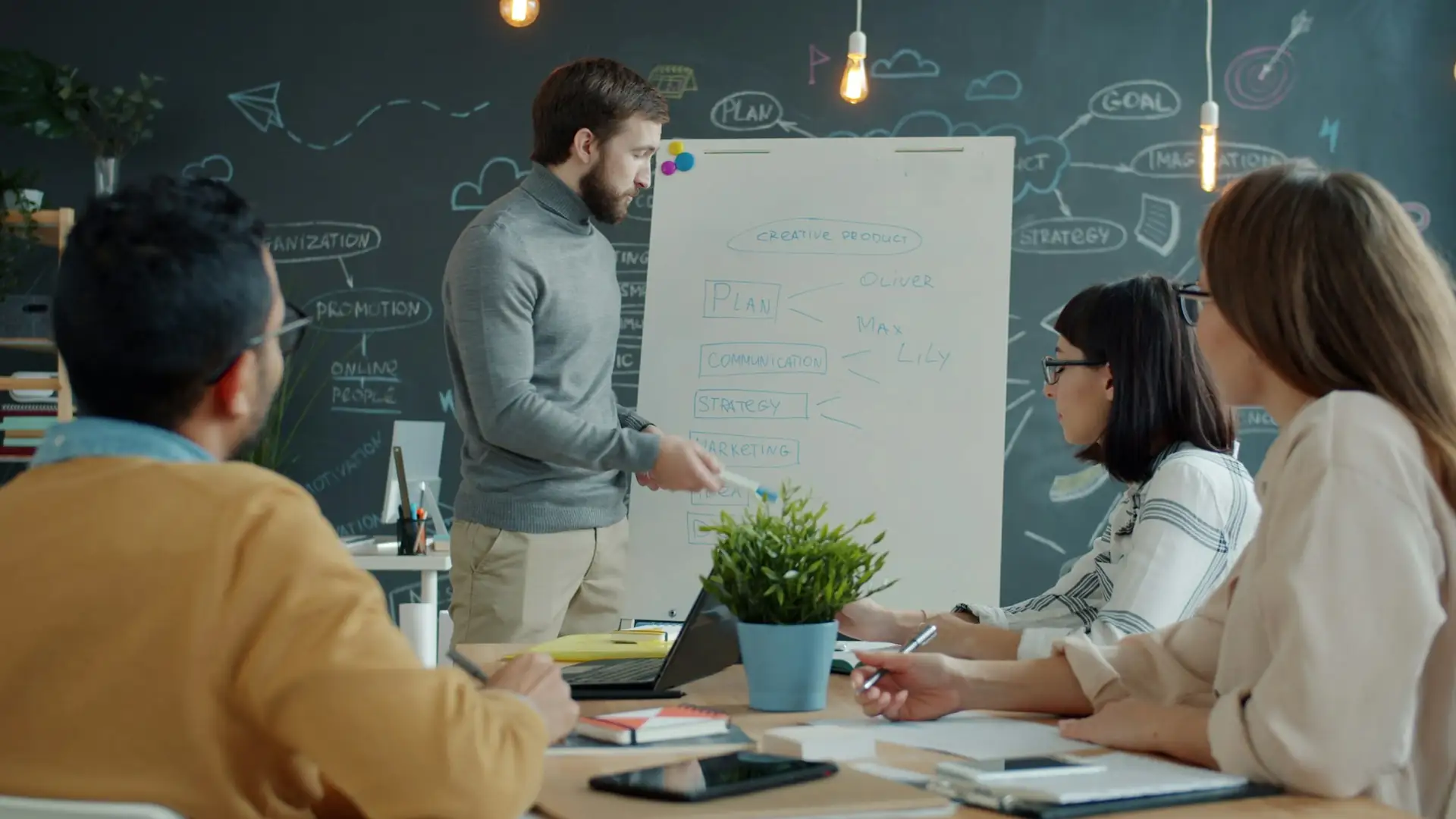 Une équipe autour d’une table pendant qu’une personne trace un plan au tableau blanc